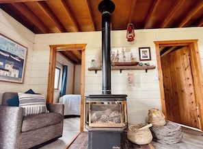 A cozy room with a wood-burning stove, a sofa, a bed, and a wooden ceiling.