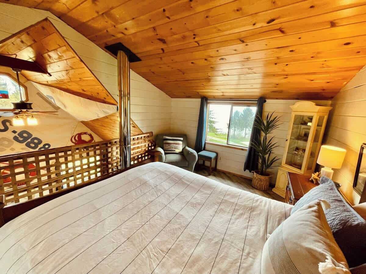 A bedroom with a large bed, a desk, a chair, a window, and a cabinet.