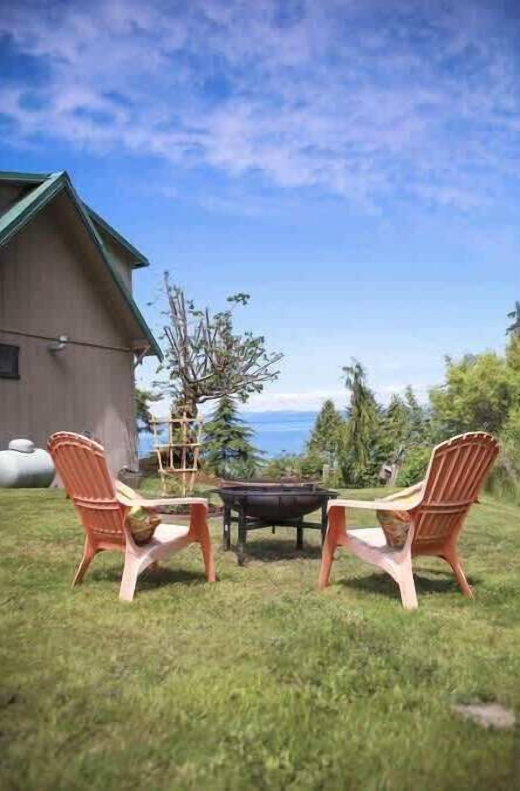 A patio with two Adirondack chairs, a fire pit, and a view of the ocean.