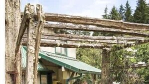 A rustic wooden structure with a green roof, a stone pathway, and a small garden area.
