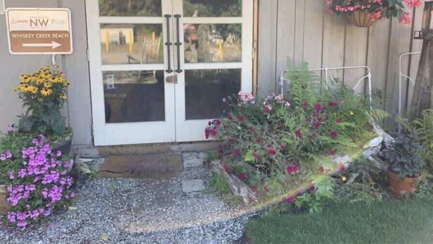 A building with a white door, a sign pointing to Whiskey Creek Beach, and various flowers and plants around the entrance.