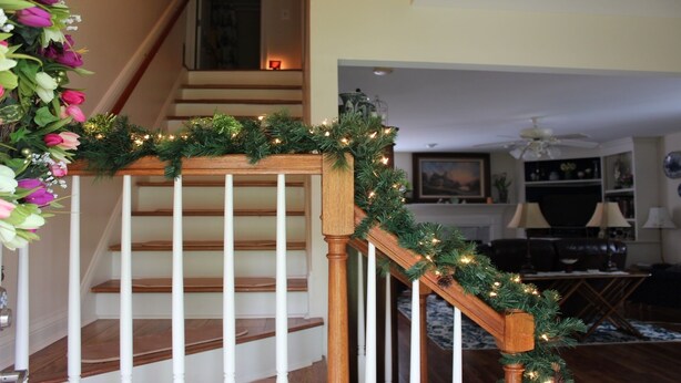 Un escalier doté d’une rampe en bois et de balustres blanches, décoré d’une guirlande de verdure et de guirlandes lumineuses.