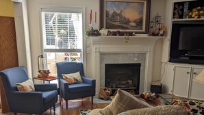 Un salon avec une cheminée, deux fauteuils bleus, un canapé beige et un téléviseur posé sur un meuble.