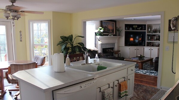 A kitchen with a central island, a dining area with a table and chairs, a living room with a sofa and a fireplace, and a hallway with a telephone.