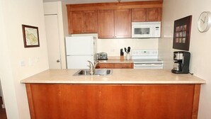 A kitchen with wooden cabinets, a white refrigerator, a microwave, a stove, and a coffee maker. - Ocean views at Kealia Resort on Sugar Beach! (Kihei)