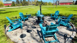 A circular outdoor seating area with six turquoise Adirondack chairs around a central fire pit.