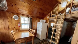 Ein Interieur einer Holzhütte mit Esstisch, Stühlen, einem Kühlschrank, einer Mikrowelle, einer Uhr und einem Fenster mit Vorhängen.