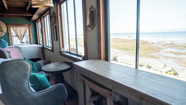 Ett rum med utsikt över stranden, ett träbord, en bekväm fåtölj och en lampa av rotting.