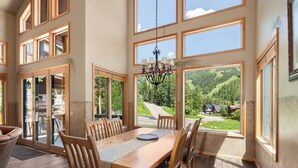 A spacious dining area with a large wooden table and chairs, large windows offering scenic mountain views, and a chandelier hanging from the ceiling. - Gorgeous Townhome Views of the Slopes, Sleeps 12, Private Baths, Private Hot Tub (Whitefish)