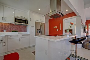 A modern kitchen with white cabinetry, a stainless steel microwave, and a red accent wall.