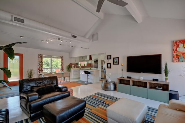 A modern living room with a black leather sofa, a TV, and a kitchen in the background.