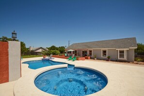 A backyard with a swimming pool, a patio with chairs, and a house in the background.