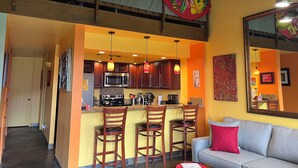 A spacious kitchen with a central island, wooden bar stools, and a grey sofa with a red pillow.