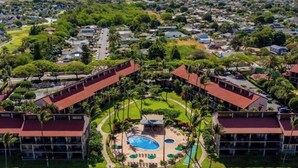A resort with a central pool, surrounded by palm trees and a view of a residential area.