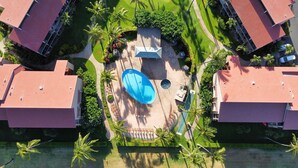 An aerial view of a residential area with a large swimming pool surrounded by greenery and palm trees.