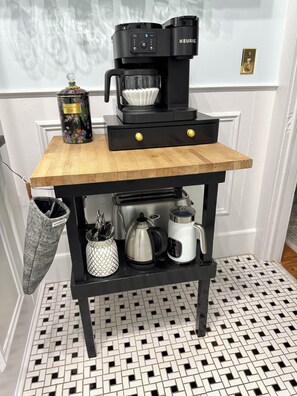 A kitchen area with a coffee maker, a kettle, and a storage cabinet.