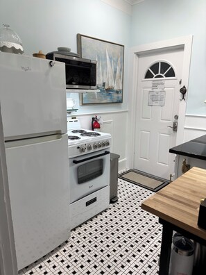A compact kitchen with a refrigerator, stove, oven, and microwave. There is a door with a window and a fire extinguisher mounted on the wall.