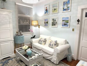 A room with a white sofa, a glass coffee table, a lamp, and framed pictures on the wall.