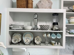 A kitchen shelf with a coffee maker, a blender, and various dishes and plates.