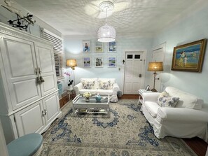 A living room with a white sofa set, a coffee table with decorative items, a patterned rug, and a chandelier.