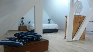 Um quarto com uma cama, um baú de madeira, um abajur e um cesto de conchas.