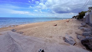 Uma praia com céu claro, costa rochosa e mar calmo.
