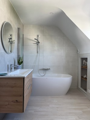 Een moderne badkamer met een vrijstaand bad, een wastafel met spiegel en een potplant.