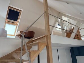 Un interior moderno con una escalera de madera, una silla marrón y una ventana con persianas.