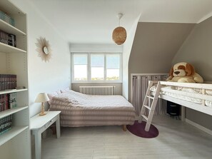 Ein Kinderzimmer mit Etagenbett, Bücherregal, Schreibtisch, Lampe, einer großen Stoffhund und einem Fenster mit Jalousien.