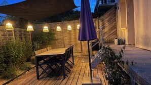 Um deck de madeira com uma mesa e cadeiras, cercado por um muro de madeira e plantas em vasos.