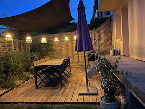 Een houten terras met een tafel en stoelen, omringd door een houten hek en plantenbakken.