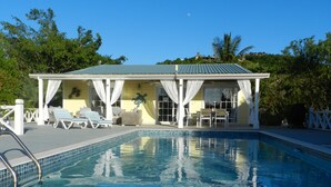 A swimming pool with a covered patio area, lounge chairs, and a view of the surrounding landscape.