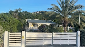 A gated entrance with a house in the background, surrounded by greenery and a clear sky.