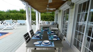 A covered outdoor dining area with a pool in the background.