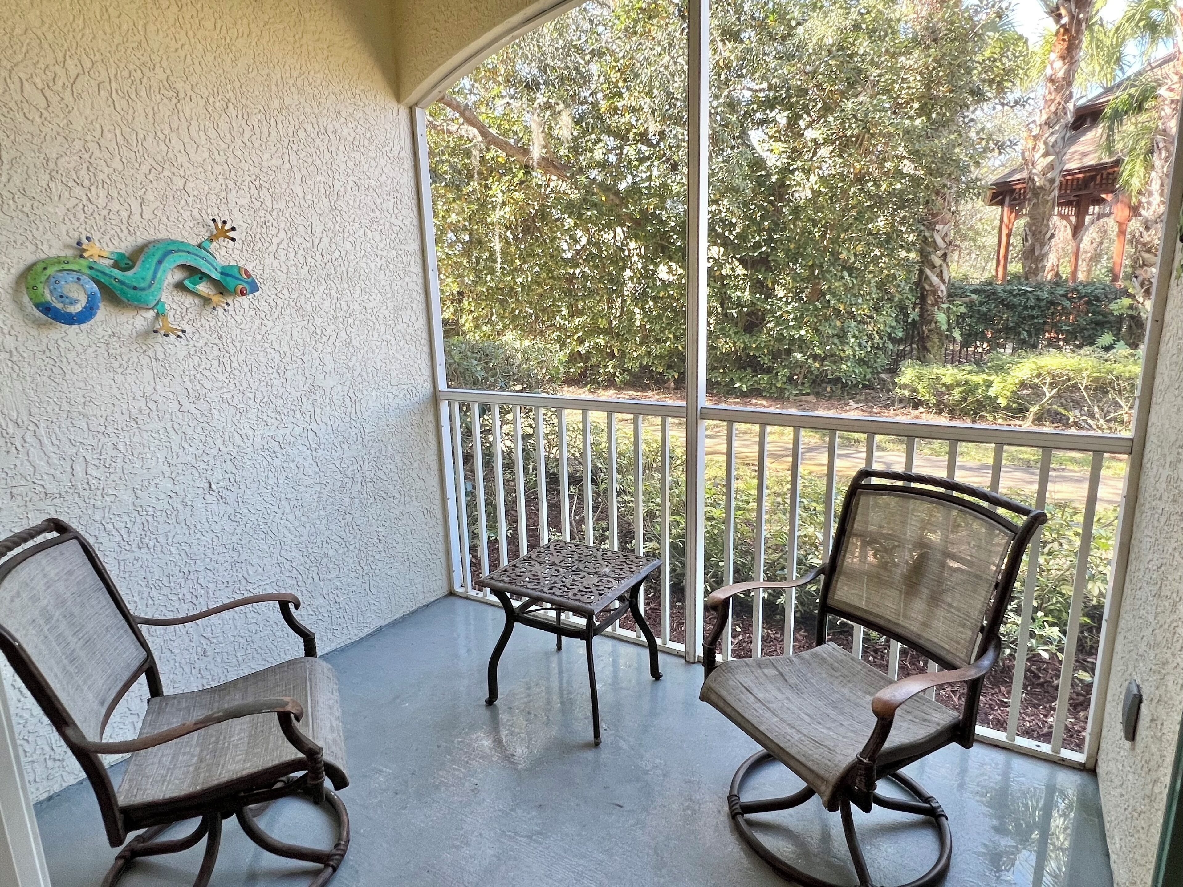 Ein Balkon mit zwei Schaukelstühlen und einem kleinen Tisch, mit Blick auf einen Garten mit Bäumen und einer Holzhütte.