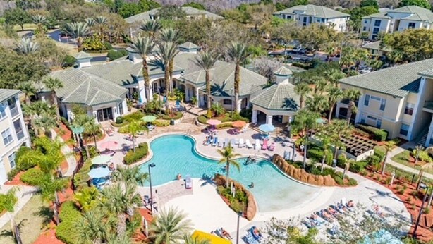 An aerial view of a resort with multiple buildings, a central swimming pool, and surrounding greenery.