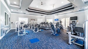 A spacious gym with various exercise equipment, large windows, and a modern ceiling design.