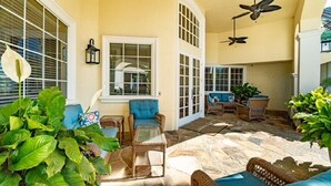 A sunlit patio with wicker furniture, stone flooring, and ceiling fans.