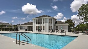A swimming pool area with a pool, lounge chairs, and a building with large windows. -  Gulf Shores - AFFORDABLE BEACH VACATION (Gulf Shores)