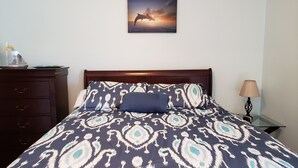 A bedroom with a patterned bedspread, a wooden headboard, a nightstand with a lamp, and a dresser with drawers. -  Gulf Shores - AFFORDABLE BEACH VACATION (Gulf Shores)