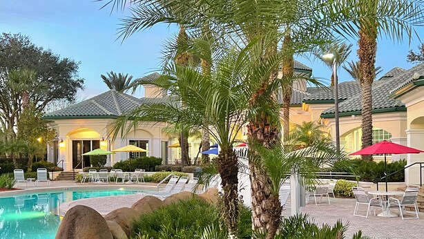 Un área de piscina con sillones, palmeras y sombrillas.