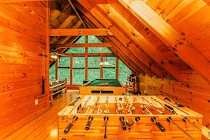 A wooden-floored room with a foosball table, a pool table, and a billiards table.