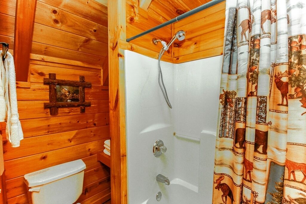 Een houten badkamer in een chalet, met een douche, toilet en een rustieke houten wand.