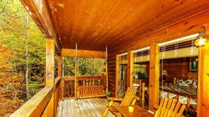 Eine Holzterrasse mit Schaukel, Holzstühlen und einem Tisch.