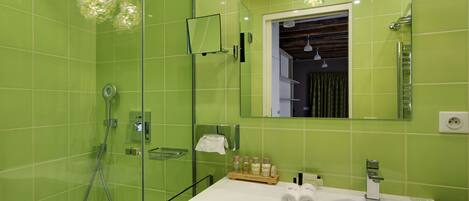 Un baño moderno con azulejos verdes, cabina de ducha de vidrio, lavamanos blanco y espejo sobre el lavamanos.