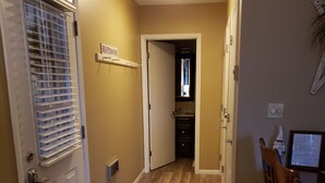 Un couloir avec une porte donnant sur une salle de bain, un petit coin cuisine et une table à manger avec des chaises.
