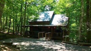 Une cabane rustique dotée d’un porche abrité et d’un escalier menant à l’entrée, le tout entouré d’une forêt dense.
