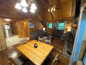 Un interior de cabaña acogedor con una mesa de comedor de madera, dos sofás, una zona de cocina y una escalera.