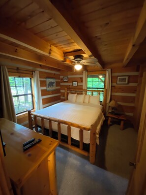 Una habitación de cabaña de madera con una cama, un escritorio y un ventilador de techo.