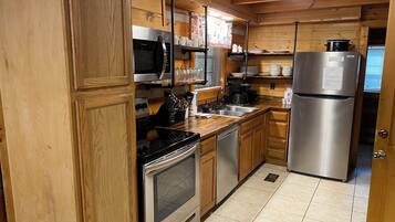 Una cucina compatta con mobili in legno, un frigorifero in acciaio inossidabile, un forno a microonde, un forno e un lavello.